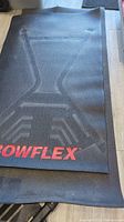 Folded black Bowflex rubber gym mat showing embossed patterns and red Bowflex logo.