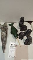 Group photo of six stone figurines including a kayak with seated figure holding paddle, green bird on stick, and four smaller animal or human shaped figures.