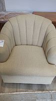 Front view of beige swivel tub chair showing channel tufted back and cushioned seat.