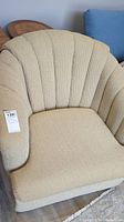 Front view of beige swivel tub chair showing scalloped backrest and seat cushion