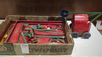 Photo of box with various Meccano metal parts, including strips, plates, wheels and small components.