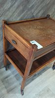 Photo showing the wooden tea trolley from an angle highlighting the drawer and lower shelf with metal handles and wood grain.