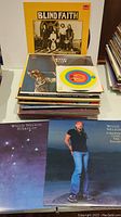 Stack of various vinyl records including Blind Faith LP album on top, Woody Allen LP album beneath, and a 45 single by Rolf Harris in paper sleeve showing Capitol label.