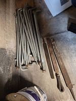 Multiple L-shaped 3/4 inch threaded steel anchors and three metal files laid on concrete floor.