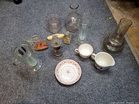 Overview of assorted antique and vintage glassware and ceramics on grey carpet