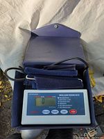Overall view of the digital blood pressure monitor in its open blue carrying case, showing the cuff and main device display.