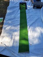 Full length image of the putting green and ball return unit showing the turf and the electric cord.