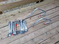 Folded metal fire escape ladder with attached chains and red-capped hooks laid out on a wooden deck.