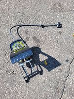 Foot air pump with gauge, showing the gauge, textured foot pedal, and hose on asphalt surface.