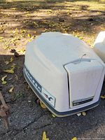 White plastic cowl hood for a Johnson 10 HP motor showing overall shape, decals and logos in daylight outdoors on ground.
