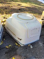 Full view of off-white Johnson Super Sea-Horse boat cowl placed on the ground with leaves around, showing overall shape and top hatch area.