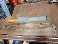 Large sharpening stone with wooden handle and leather sleeve placed on a wooden surface