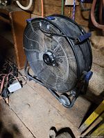 Full view of the fan showing the metal mesh grille, wheels, blue handle grip, and frame