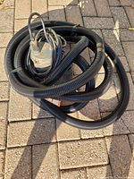 Mastercraft metal submersible sump pump with black corrugated hose coiled around it sitting on outdoor paving.