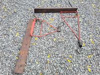 Photo showing two dark wooden 2x6 planks with attached red metal brackets on gravel ground.
