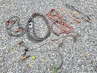 Photo showing various wires, jumper cables, and power cords spread on gravel surface