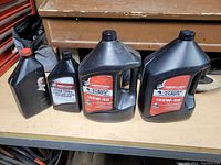 Four plastic bottles of Mercury gear lubricants on a shelf, including two SAE 85W-40 bottles, one premium gear lube bottle, and an older style bottle with a damaged label.