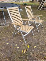 Photo showing two foldable outdoor chairs placed on grass, both with wooden slats and metal frames.