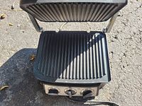 Open electric panini press showing ridged grill plates on both top and bottom halves.