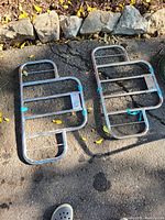 Two stainless steel racks laid on pavement with rocks in the background, secured with blue plastic ties.