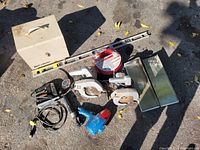 Various tools arranged on the ground including two circular saws, a blue power tool, a metal toolbox, extension cord, and a metal level.