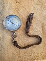 Photo of circular vintage compass with clear markings and attached leather strap laid on wooden surface