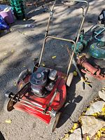 Full view of vintage red metal lawn mower with engine and handlebar, showing wheels and deck, with some wear and dirt.