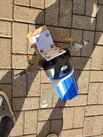 Top front view of the water filter system showing attached metal mounting bracket, blue and black plastic housing, valves, and plastic wrench.