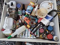 Top-down view of wooden bin containing various home maintenance products like spray cans, bottles, tubes, belts, and a funnel.
