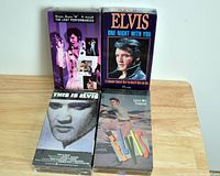Four Elvis Presley VHS tapes arranged on a wooden surface. Titles visible on box fronts: The Lost Performances, One Night With You, This Is Elvis, and Love Me Tender.