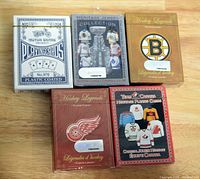 Five sealed decks of playing cards displayed on a wood surface: one standard Motor Brand deck and four NHL hockey-themed decks including Heritage Jersey Collection, Boston Bruins, Detroit Red Wings, and Team Canada Heritage designs.
