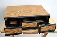 Top view of the cassette holder showing three pull-out drawers with woodgrain fronts and black interiors.