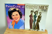 Photo showing both music tab books - The Supremes Greatest Hits and Patsy Cline on a wooden surface against a plain background.