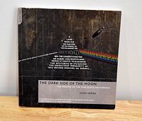 Front cover of The Dark Side of the Moon soft cover book showing the album's iconic prism graphic and title text.