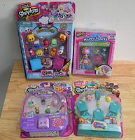 Four Shopkins toy packages displayed on a wooden table, including Season 6 Chef Club 12-pack, Happy Places single figure set, large 36-pack, and a 5-shopkins multi-pack with display bases.