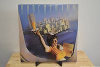 Front cover of Supertramp - Breakfast In America vinyl LP showing artwork with waitress and breakfast cityscape with some edge and spine wear visible.