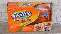 Front of the Swiffer Carpet Flick Sweep Starter Kit box showing branding, key features, and orange sweeper inside.
