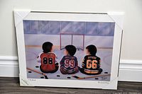 Full view of the plaque showing three children in hockey jerseys sitting on ice facing a goal, mounted on a 20" x 16" board with corner protectors.