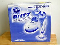 Photo of the front of the Tide Buzz Ultrasonic Stain Remover box showing product name and image of the device and its accessories.