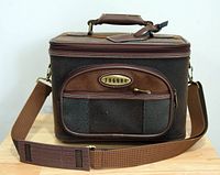 Front view of the vintage Jaguar brown travel case, showing the textured exterior, front zippered pocket with Jaguar logo, top handle, and adjustable shoulder strap with shoulder pad.
