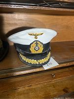 Lot showing a white-topped German military hat with black brim and gold eagle insignia on front.