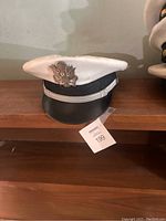 Front view of a white US Navy officer hat with silver eagle insignia and black chin strap.