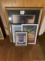 Photo showing four framed prints leaning against a wall, including the aviation and artistic prints.