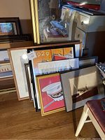 Group of framed artworks leaning against a wall and mirror, showing diverse styles and frame finishes