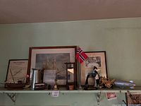 Photo of shelf showing various decor items including framed paintings, model ships, figurines, and decorative metal and ceramic objects.