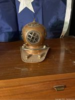 Front view of the bronze decorative diver helmet on wooden surface with a folded flag in the background