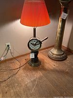 Lamp with engine operator telegraph base turned on on wooden floor next to another brass item.