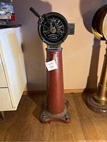 Front view of pedestal-mounted engine order telegraph showing full height and red painted base