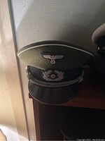Single green WWII military hat with visible silver eagle insignia on front and white trim along the edge, placed on a wooden surface.