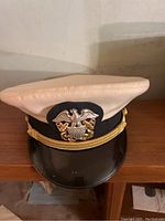 White top US Navy officer hat with gold eagle and anchors insignia and black visor